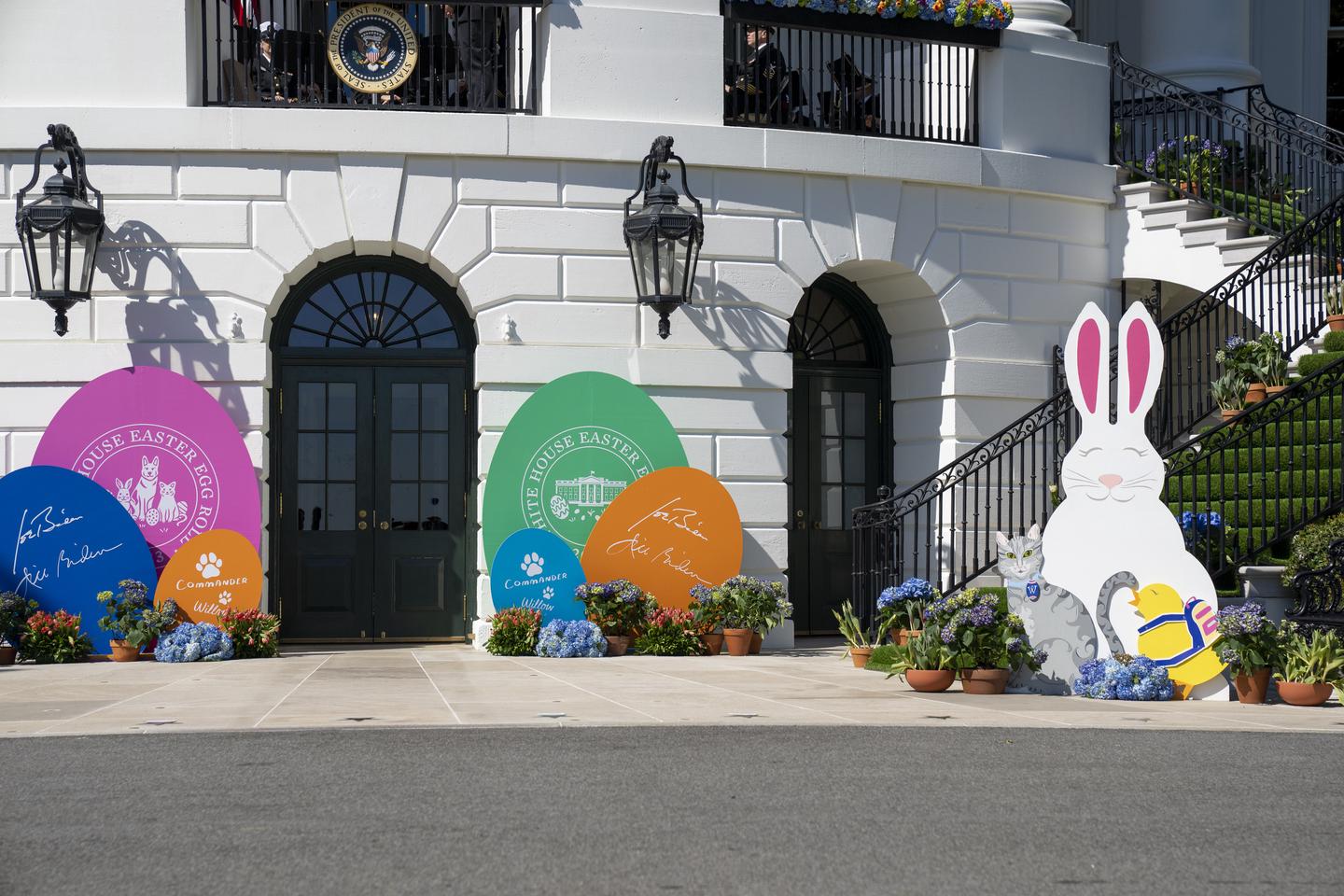 White House entry point, complete with a staircase on the right, a large bunny cutout, a cat cutout, and baby chick cutout. Other decor includes several large egg cutouts indicating to the White House Easter Egg Roll and signatures of President Joe Biden & First Lady Jill Biden. Decorations for Easter Egg Roll event at White House entry point