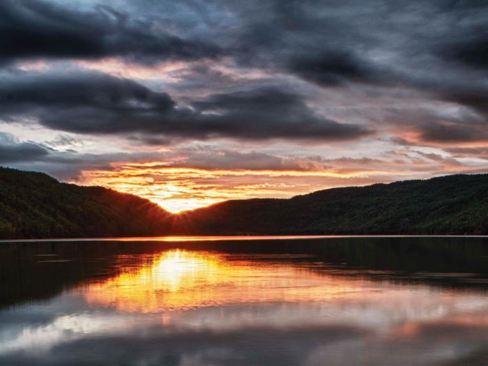 Sun sets behind the mountains looking over a mirror-surfaced lake.Sunsets from the boat launch or day use waterfront at Hidden Lake Campground are not to be missed.