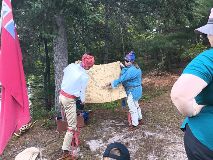 Two park rangers dressed as French Voyageurs reference a map during a North Canoe program