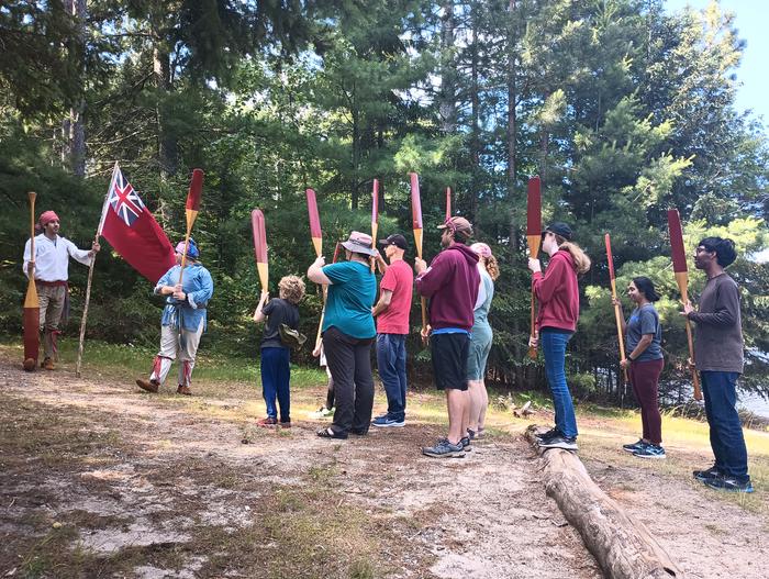 Rangers dressed as French voyageurs stand in front of visitors holding paddles.Rangers dressed as French voyageurs give a North Canoe program to visitors.