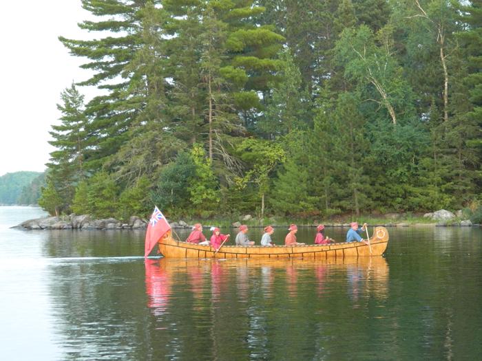 Visitors paddle a 26-foot replica of a birch bark north canoe on a calm lake.Visitors paddle a 26-foot replica of a birch bark north canoe.