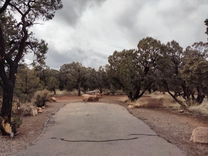 Parking spot for a campsite, surrounded by trees and scrubs.Site 6 has two tent pads, a picnic table and a metal fire ring. The site is surrounded by pinon-juniper trees.