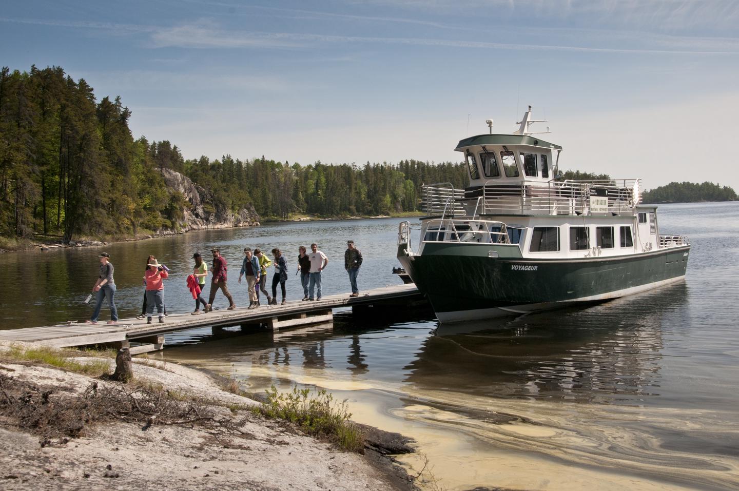 The Voyageur tour boat docked at the Anderson Bay Trailhead and visitors walking on the dock