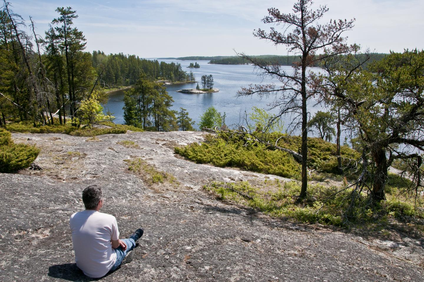 A sits atop a granite overlook enjoying the lake view belowA man enjoys the view from the Anderson Bay overlook 