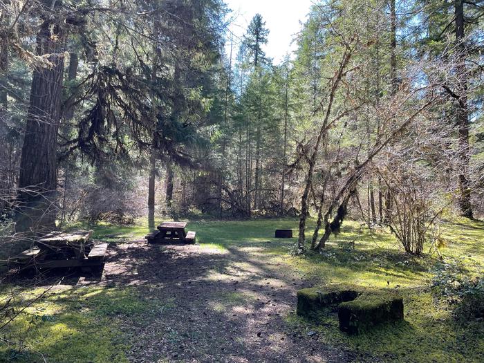 Two wooden picnic tables and two stone fire pits in a shaded, grassy area.The day use area within Sand Prairie is open to all guests free of charge. The area has several picnic tables and fire pits available, as well as convenient access to the Middle Fork Trail.
