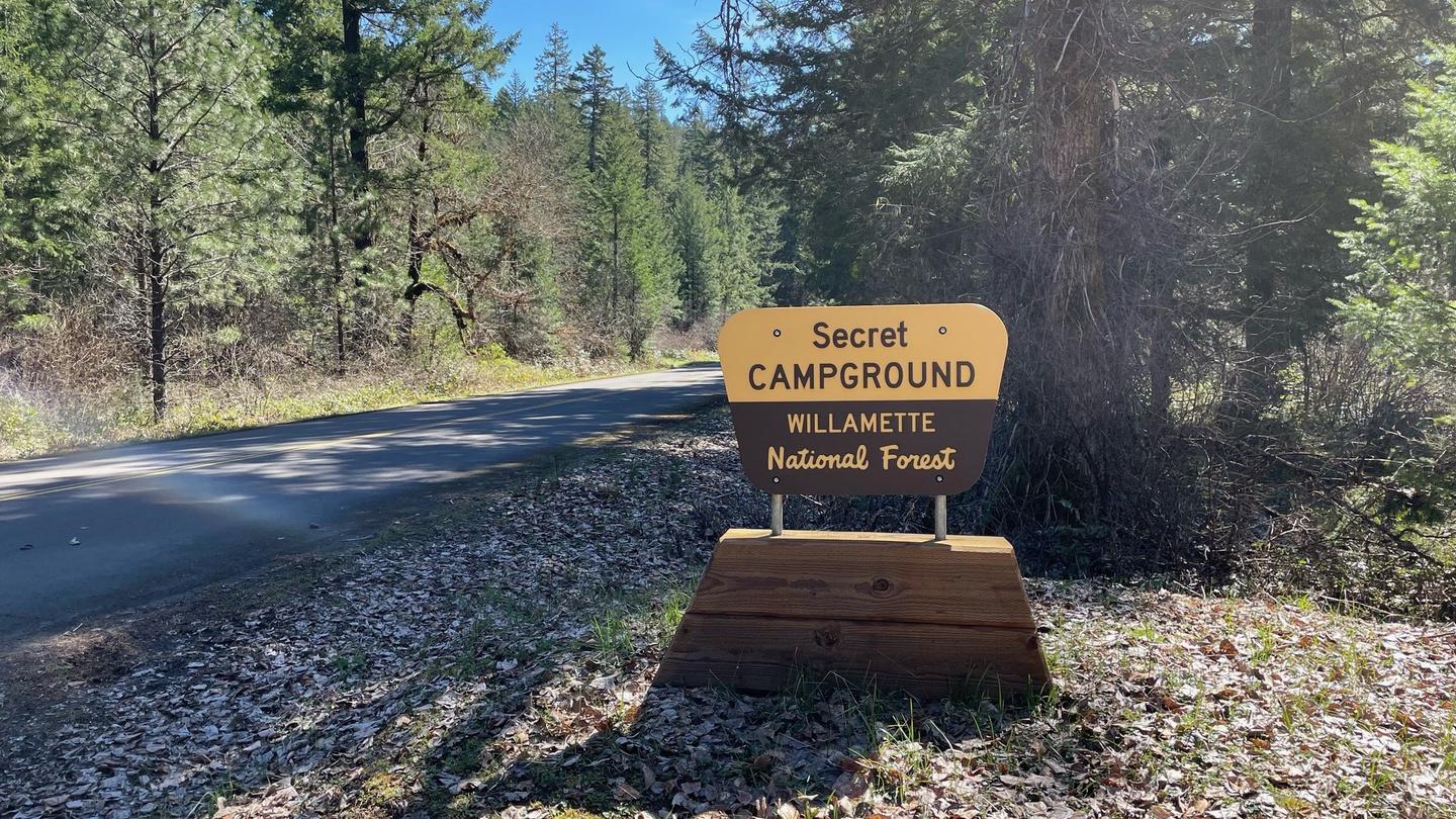 A brown and cream colored plastic sign on a wooden base. The sign reads "Secret Campground".The entrance sign for Secret Campground can be easily seen from Forest Service Road 21 and leads you to the campground gate.