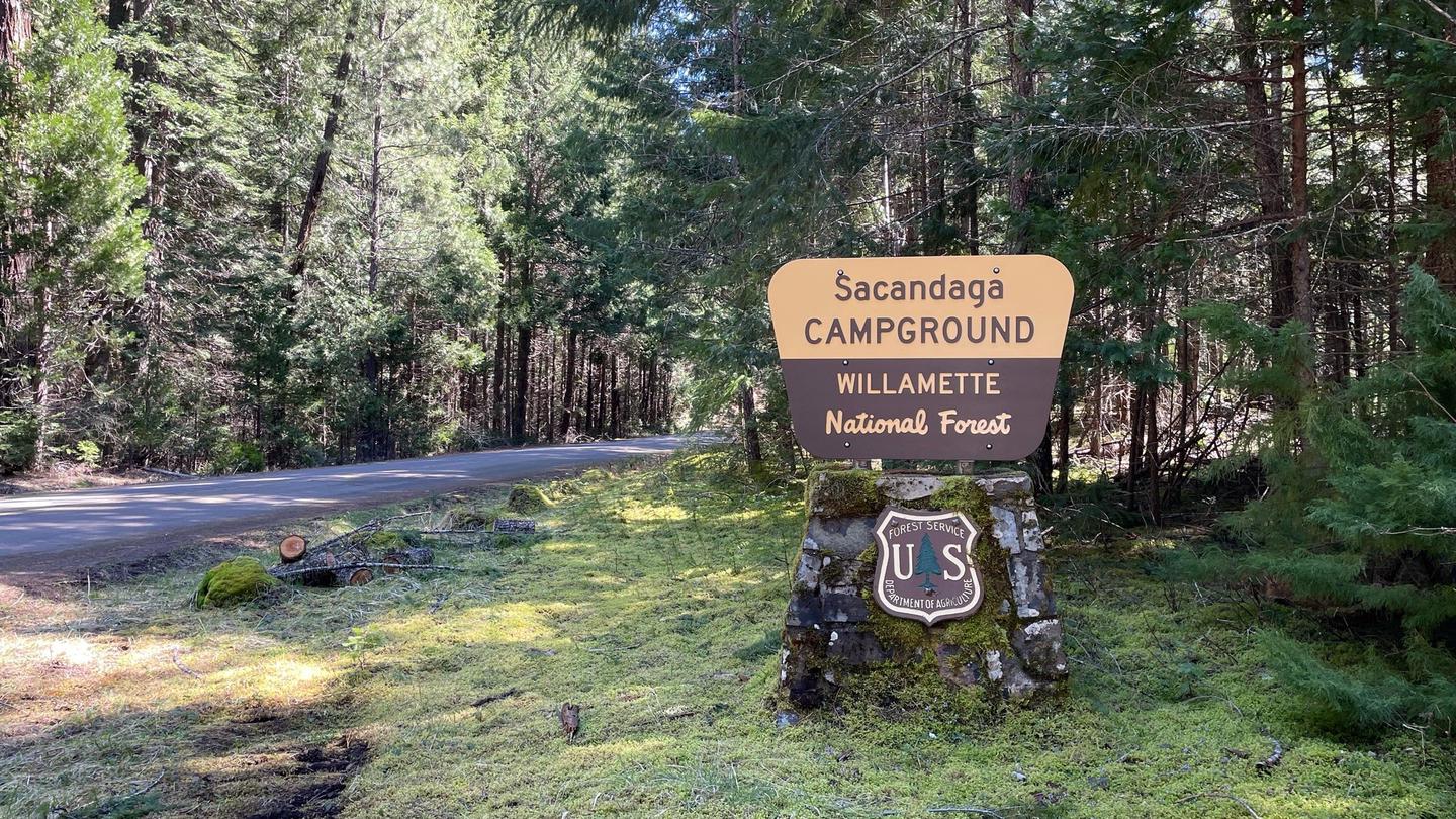 A cream and brown sign on a rock pedestal. The sign says " Sacandaga Campground".The entrance sign to the campground can be easily seen from Forest Service Road 21 and leads directly to the campground.