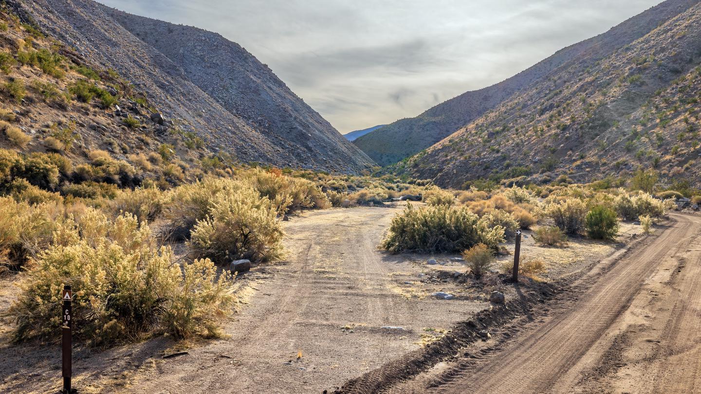 Dirt gravel road with parallel roadside campsite surrounded by mountains.