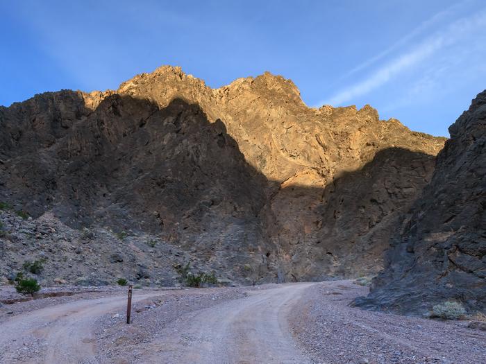 Gravel dirt road with a parallel roadside campsite surrounded by dark canyon walls.Gravel dirt road with a parallel roadside campsite. 