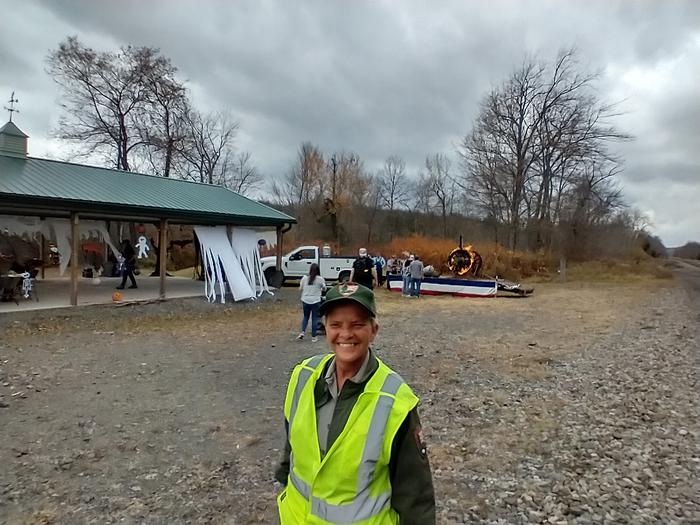 A park ranger is standing in front of a decorated pavilion. A metal ring of fire is in background.Park Ranger Pavilion & Ring of Fire