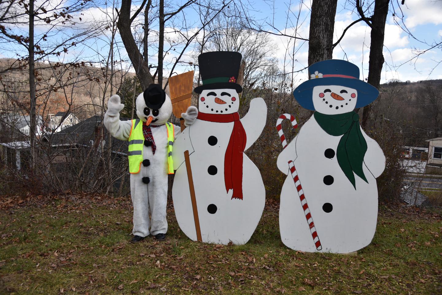 There are three snow people.  Two are large wooden displays .  One is a person in costume wearing a safety vest.Three Amigos