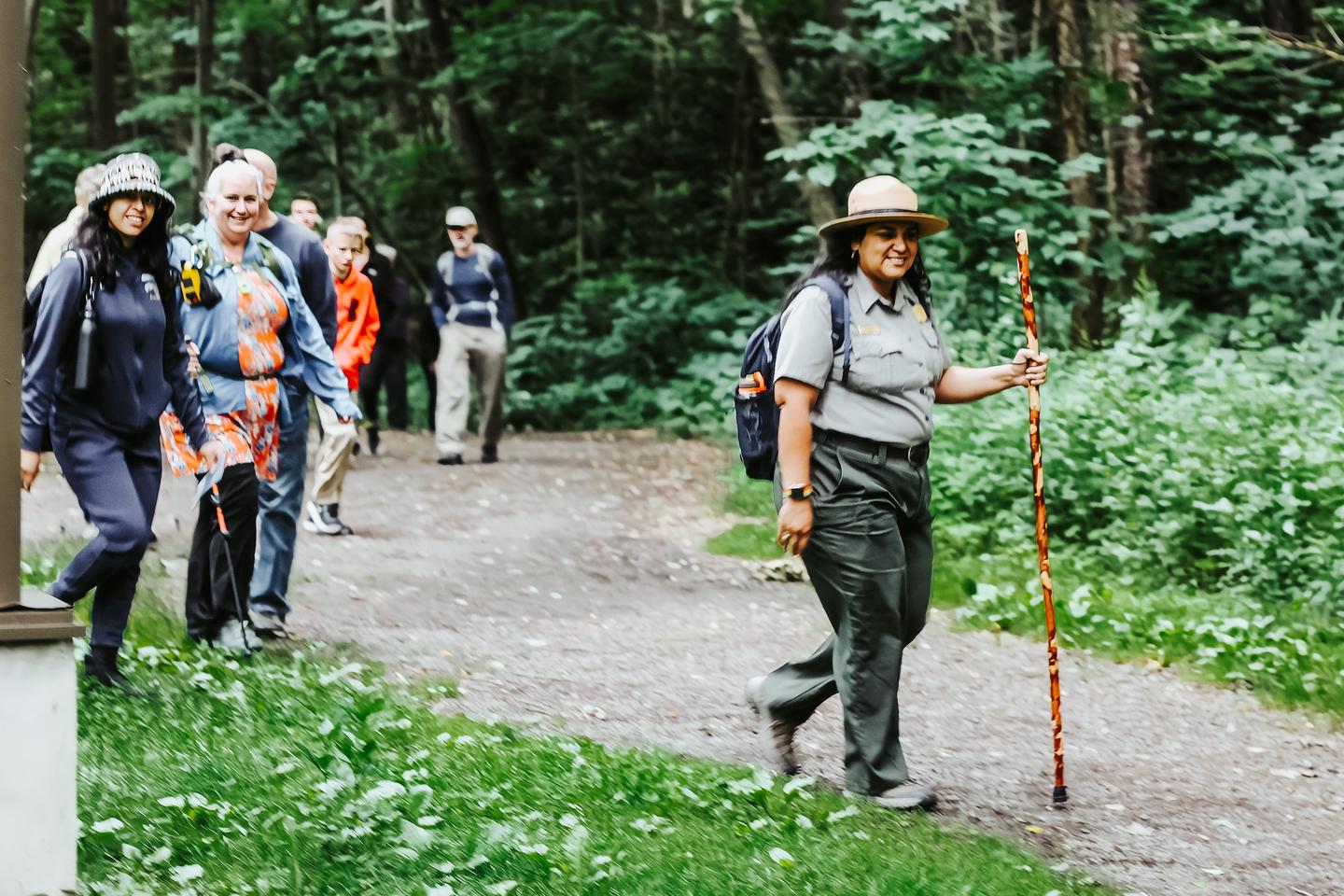 A park ranger is leading a group of hikers along a dirt train in a wooded area.Hiking the Lackawanna River Heritage Trail