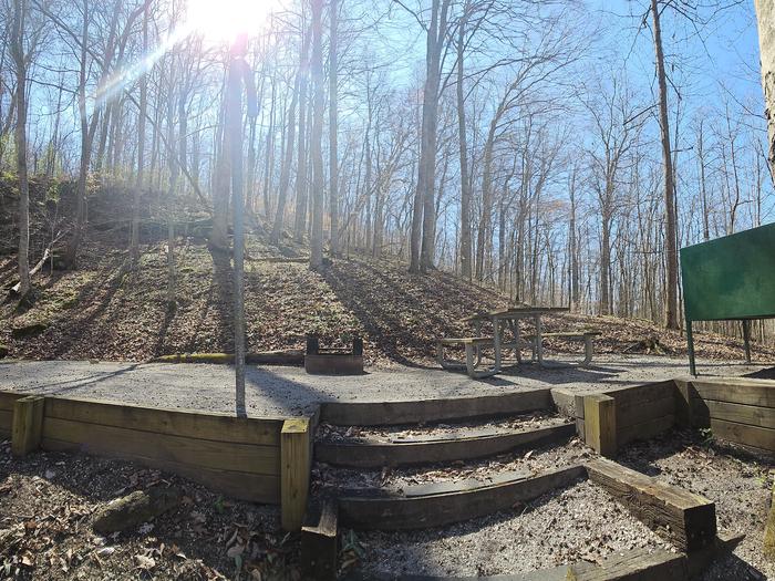 A tent site in the woods with gravel filled tent pad and wood timbers supporting the edges.Campsite 1