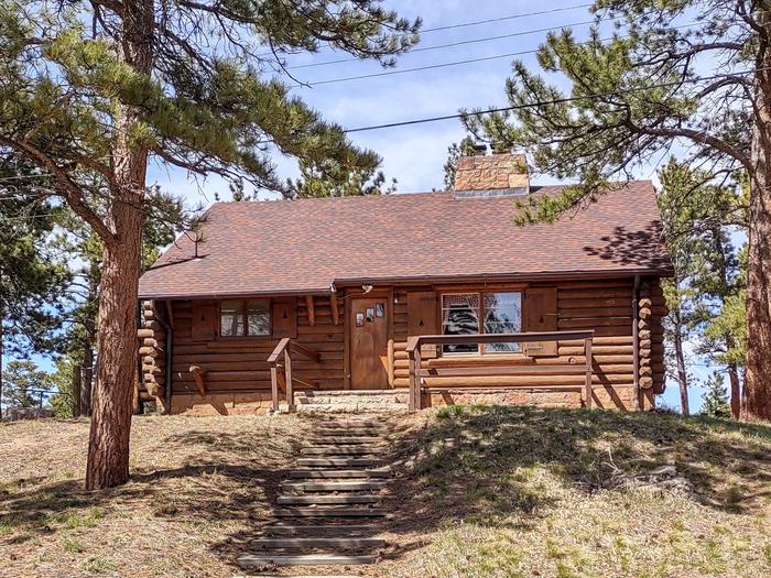 Log cabin with tree in the foreground and wooden steps up a hill. Redfeather Assistant Ranger Cabin