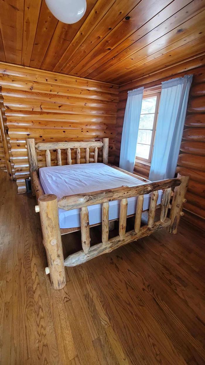 Log bed in bedroom with oak floors, log walls, and wood paneled ceiling. Redfeather Assistant Ranger Cabin one. 