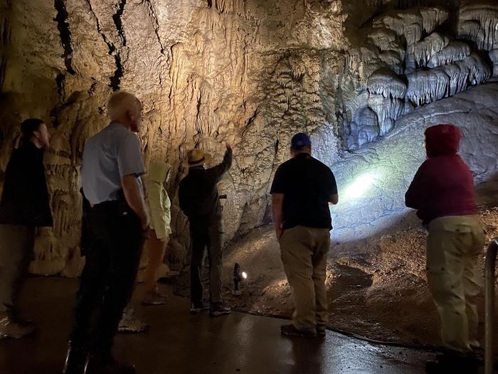 4 visitors listening to a ranger describe the surrounding flowstone found in a larger chamber of Middle CaveTour group in the Big Room of Middle Cave