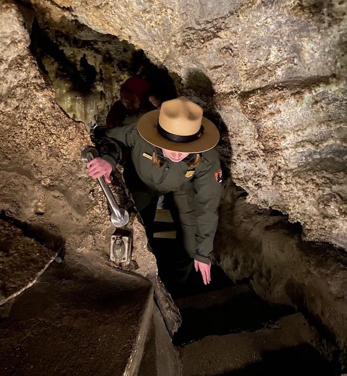 Ranger twists and ducks with the assistance of a handrail to avoid touching cave walls and the low ceiling while climbing a stairwayNavigating a narrow passageway