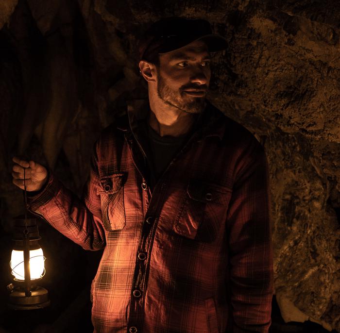 Visitor holding a lantern inside a dark caveCentennial Lantern Tour