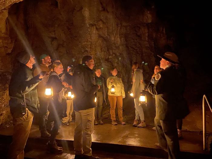 Ranger with a group of visitors each holding a lantern in a large dark cavernCentennial Lantern Tour
