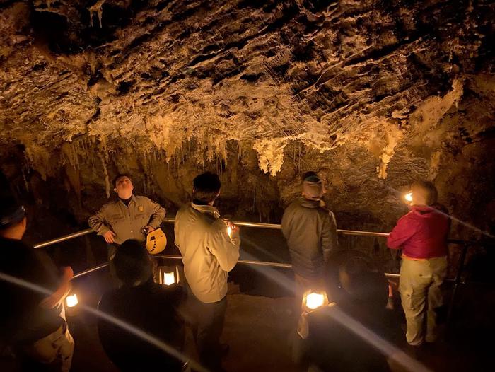 Visitors and ranger standing in a highly decorated chamber lit only by lantern lightThe Chimes Chamber by lantern light