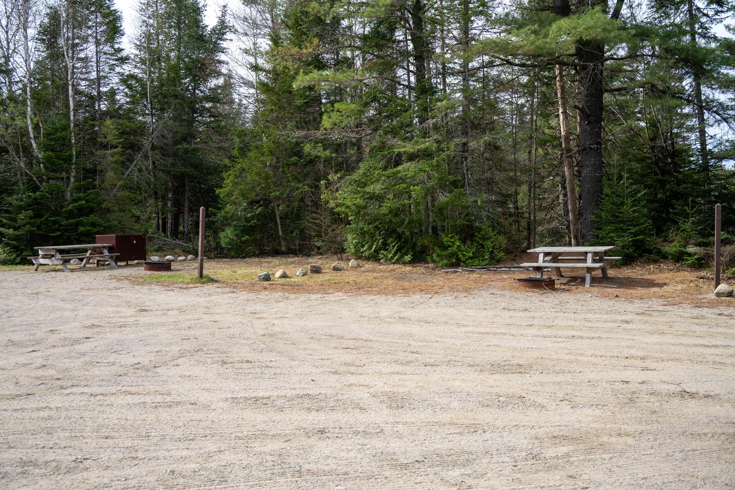 Two campsites side by side next to a gravel lot. The two sites each have a picnic table, a fire pit, and a food storage locker. A trail is next to the campsite to the left.A short hiking trail leads to a viewpoint at Sandbank Stream from the camping area.