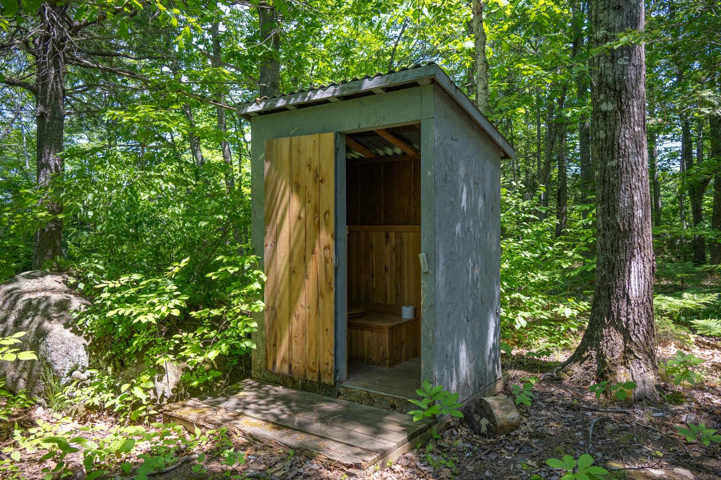A wooden pit toilet structure at the campsite with the door open on a sunny day.A pit toilet is located at the campsite.