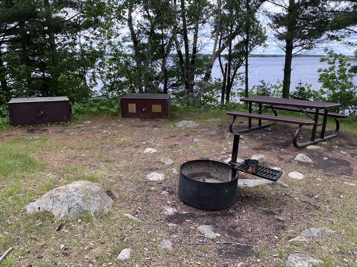 K11 - Happy Landing, view looking out from campsite of the fire ring, picnic table, and bear lockers with the water in site through the trees.K11 - Happy Landing campsite on Kabetogama Lake