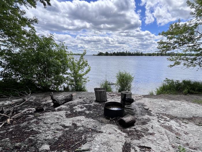K21 - Maple Point, view looking out from campsite with the fire ring on a rocky point surround by logs for seating overlooking the water.K21 - Maple Point campsite on Kabetogama Lake