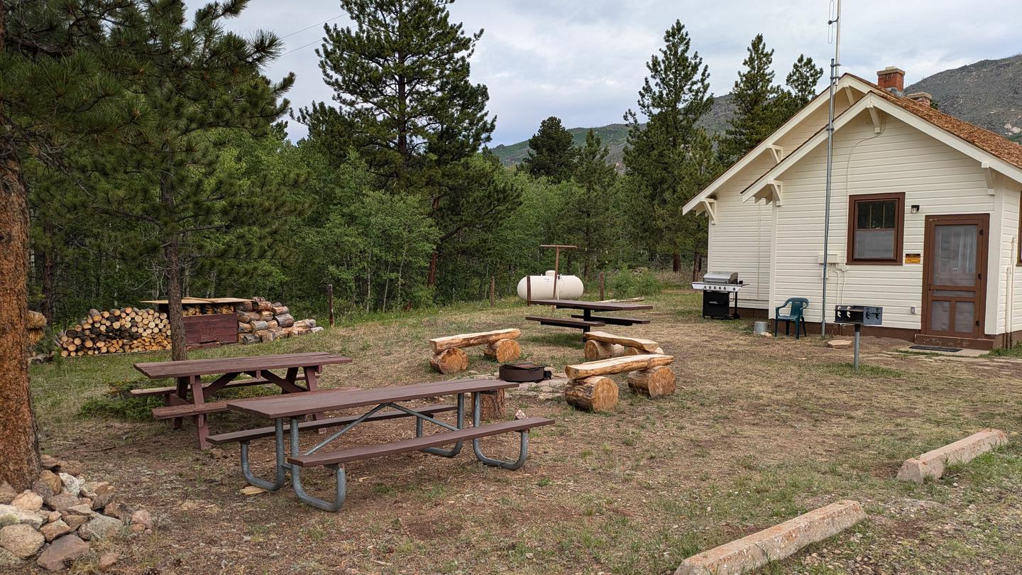 Picnic tables, firepit, firewood, grills, parking blocks, propane tank and Ranger Cabin with pines and aspen trees in background.Ranger Cabin showing fire pit and picnic tables. 