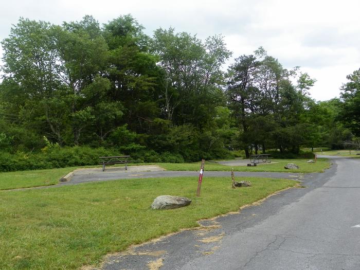 Campsite C128 has a driveway that slopes up into the site next to a picnic table, fire ring, and tent pad.