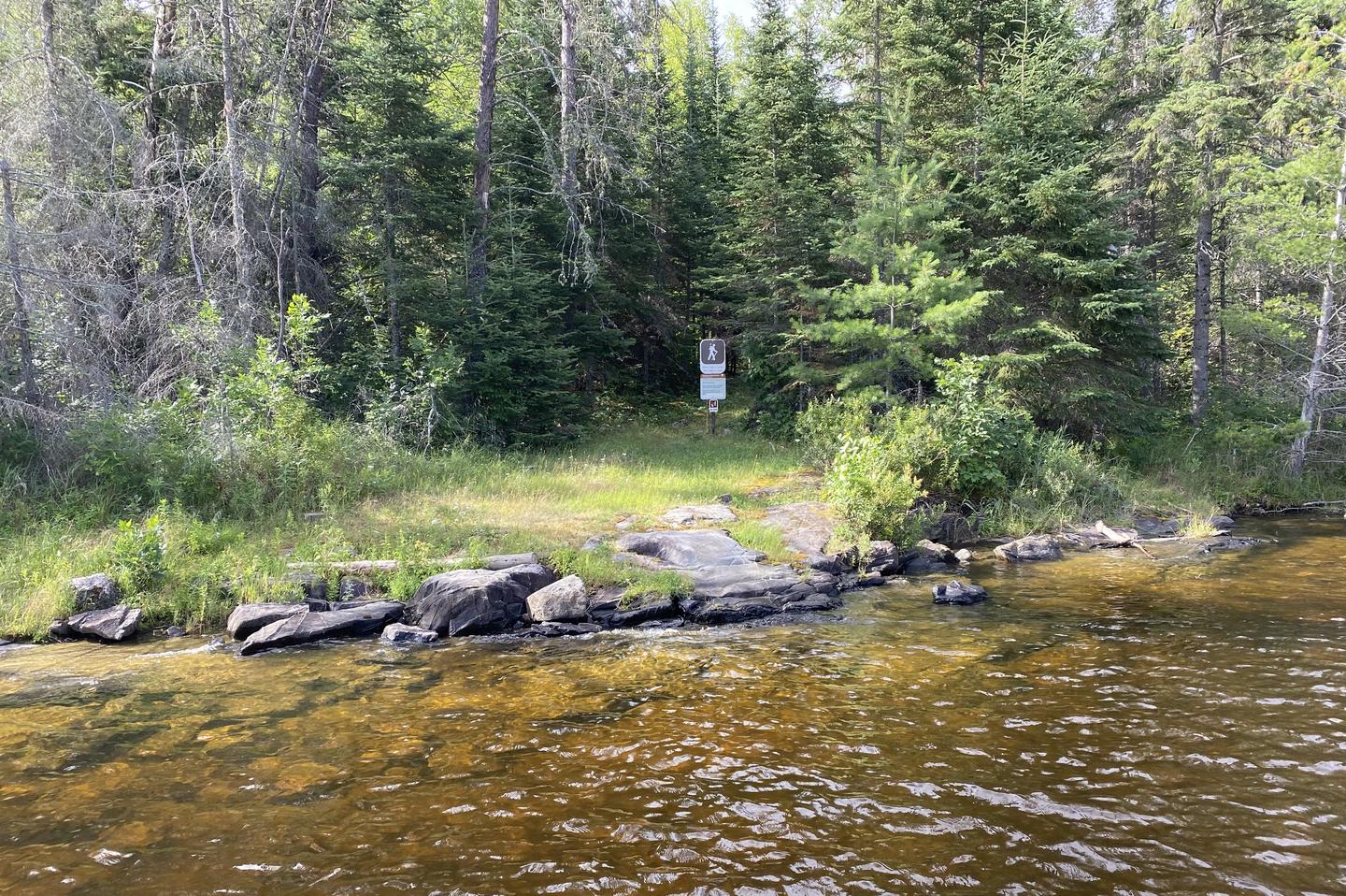 Trail head landing from water with the trail sign on shore with trees in the backgroundTrail head from water