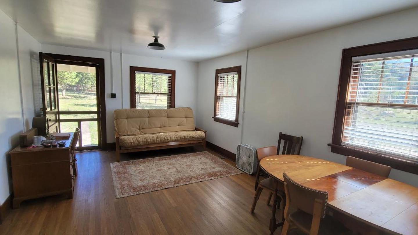 A photo of the living room in the Ranger cabin showing a table and chairs, a futon, rug, and desk. 