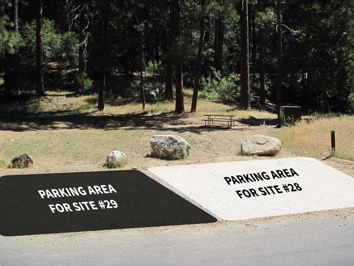 Grassy hillside with gravel parking area at the bottom of it. The parking area is shared with multiple cars for multiple sites. Overlayed on the image are a black box and white box. The white box indicates the parking area for campsite 28, the black box indicates the parking area for campsite 29.The parking area is shares between campsites 28, 29, and 30. Parking will fit two vehicles