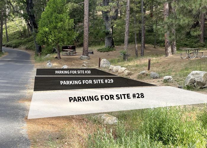 Gravel parking area in front of a hill side with campsites. The parking is shared for multiple sites. Overlayed on the image and 2 black boxes and 1 white box. The black boxes indicate the parking areas for sites 29 and 30. The white box indicates the parking area for site 28Parking is shared for sites 28, 29, and 30. Site 28 will only fit two cars. Must be pulled straight forward into the parking spot.