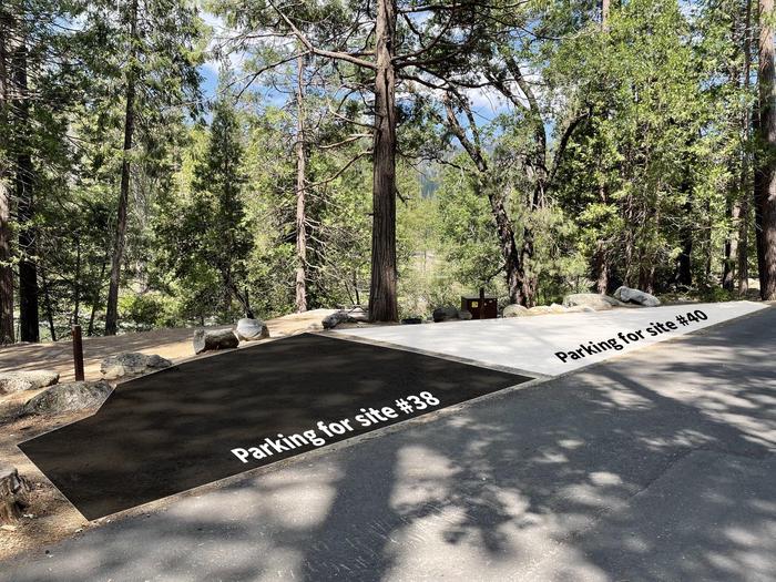 A dirt parking pad is marked by rocks next a paved road. In the background are trees and the campsite itself. Overlayed on the image are a black box and a white box. The black box indicates the parking area for site #38. The white box indicates the parking area for site #40.Parking is shared with site #38. 2 vehicles will fit in the parking space for #40. Expect vehicles to be parked close together.