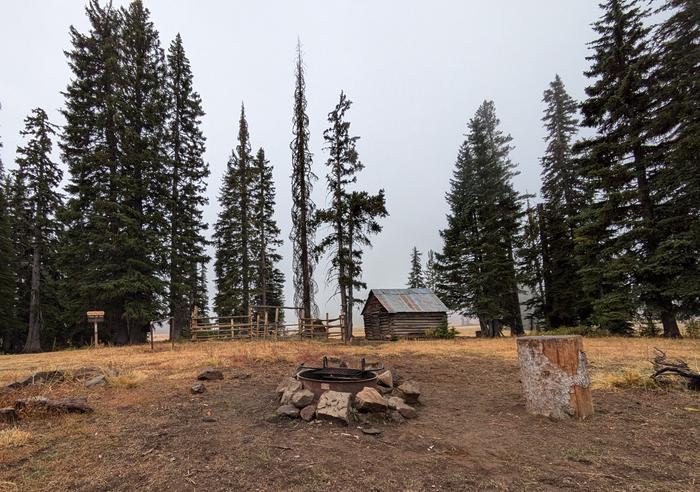 Fire pit and corral, small shed and trail sign in the background. Fire ring, corral, and trail sign at Buck Park Cabin.