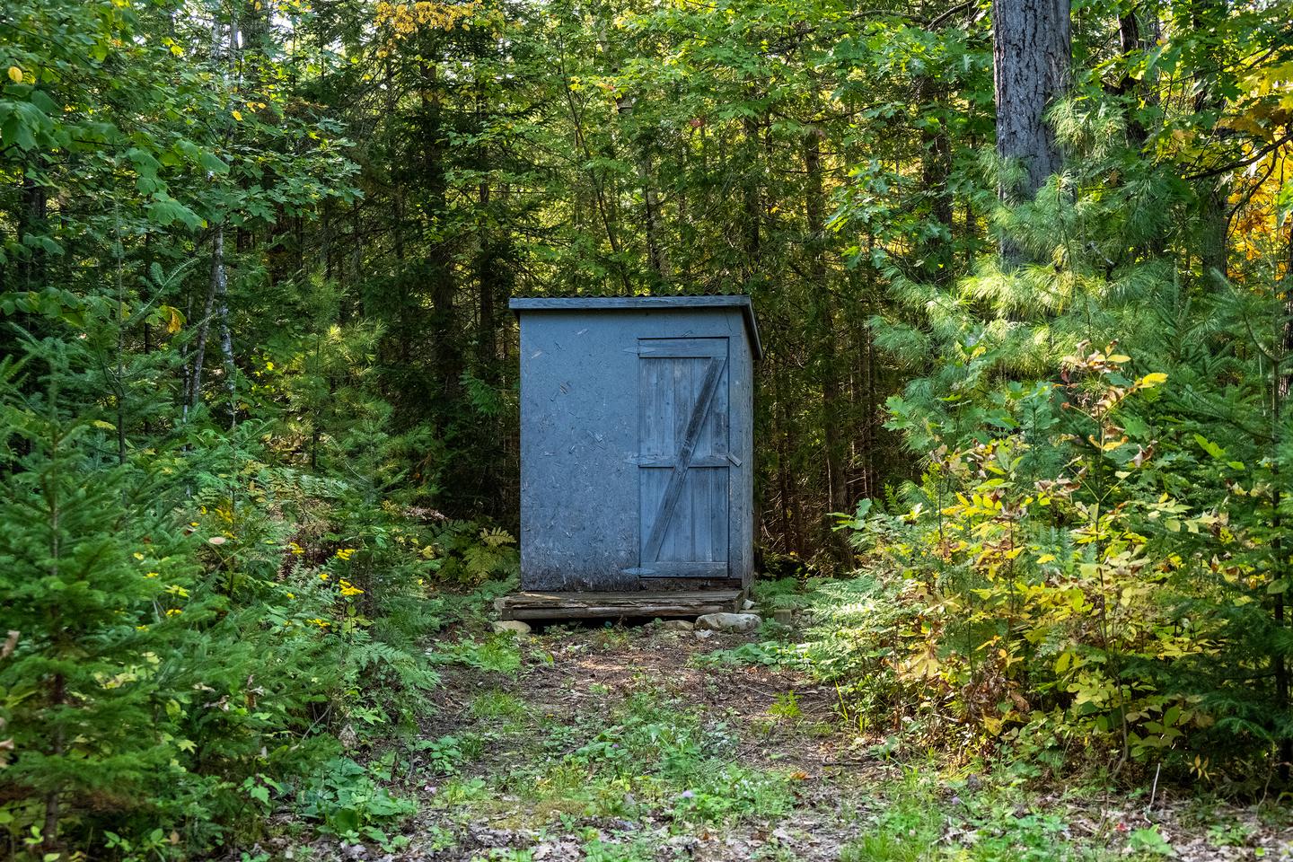 A wooden pit toilet structure at the campsite with the door open on a sunny day.A pit toilet is located at the campsite.