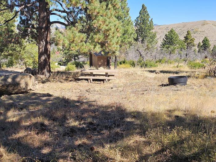 Picnic table and fire ring with vault toilet in the backgroundPrice Canyon campsite 10