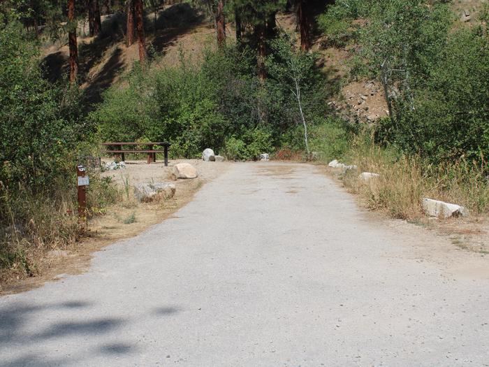 Site 15 trailer pad through trees. Site post is visible in front of bushes Site 15 trailer pad, Mountain View Campground, Boise National Forest