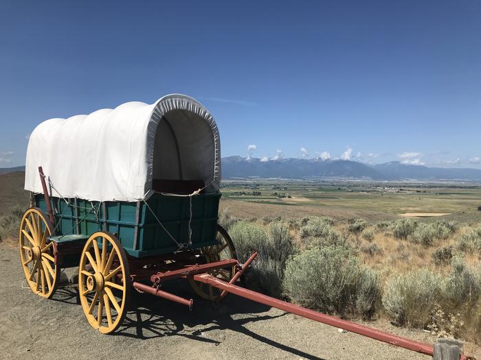 Covered Wagon with blue box and yellow wood tires in front of mountains in the backgroundCovered Wagon in the wagon encampment