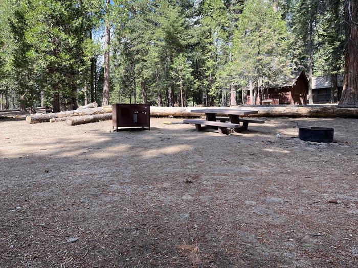 Tent pad clearing showing bear box, fire ring, picnic table and nearby restroomTent pad clearing