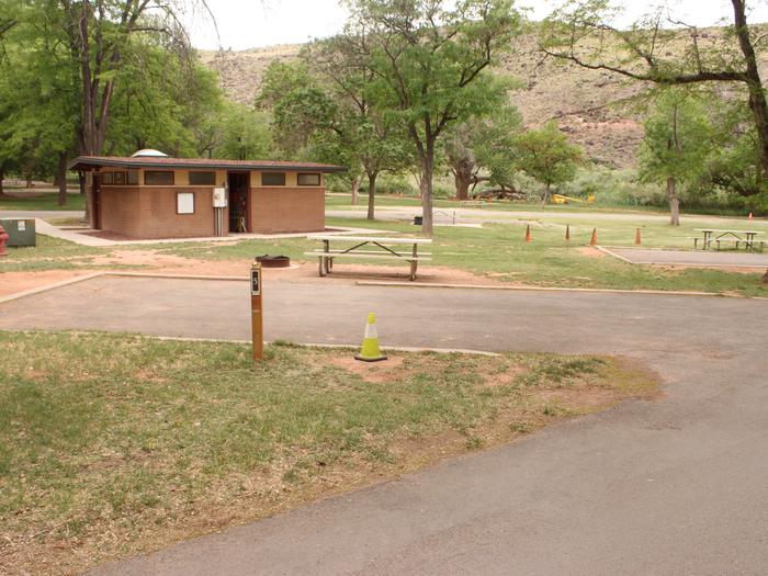 A paved driveway. Facing the end of the driveway, a picnic table is off to the right side and a fire pit is directly behind it. A small building is in the background.Site 5, Loop A in summer.
Paved Dimensions: 15' x 32'