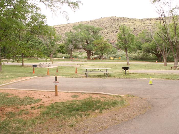 A paved driveway. Facing the end of the driveway, a picnic table and grill are off to the right side.Site 7, Loop A in summer. Admin Site.
Paved Dimensions: 20' x 33'