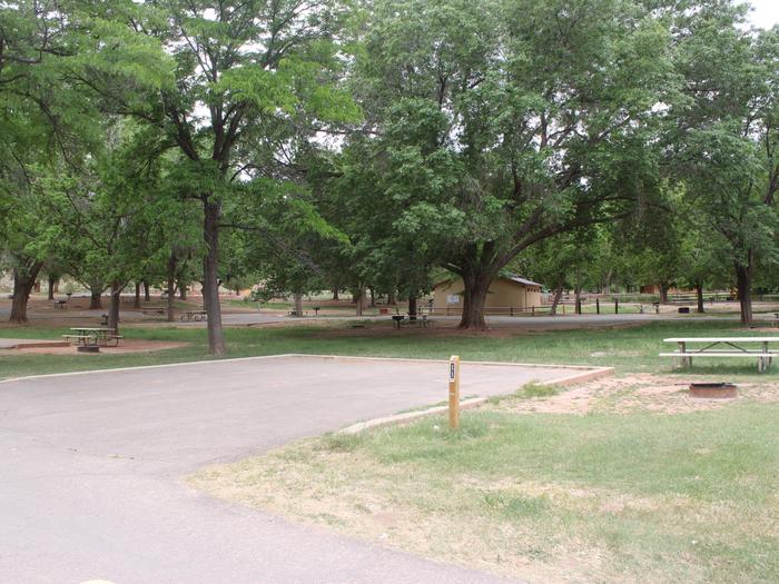 A paved driveway. Facing the end of the driveway, a picnic table and fire pit is fire pit is on the right side. A small building is in the background.Site 11, Loop A in summer.
Paved Dimensions: 31' x 31'