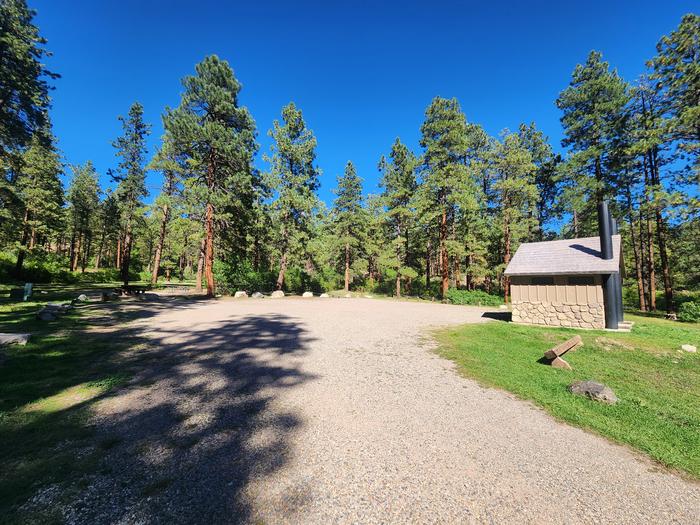 Site 1 parking area, with vault toilet, and picnic tables under pine trees