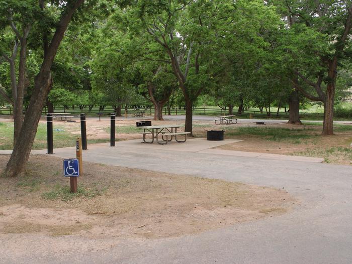 A paved driveway. Facing the end of the driveway, three bollards are in the ground at the end of the site spaced far enough apart for a bicycle to get through. To the right side there is a picnic table, grill ,and raised firepit all on pavement. A sidewalk leads from the picnic table to the left of the site. To the left side of the driveway there is a tree. Site 26, Loop B in summer. Accessible site.
Paved Dimensions: 16' x 29'