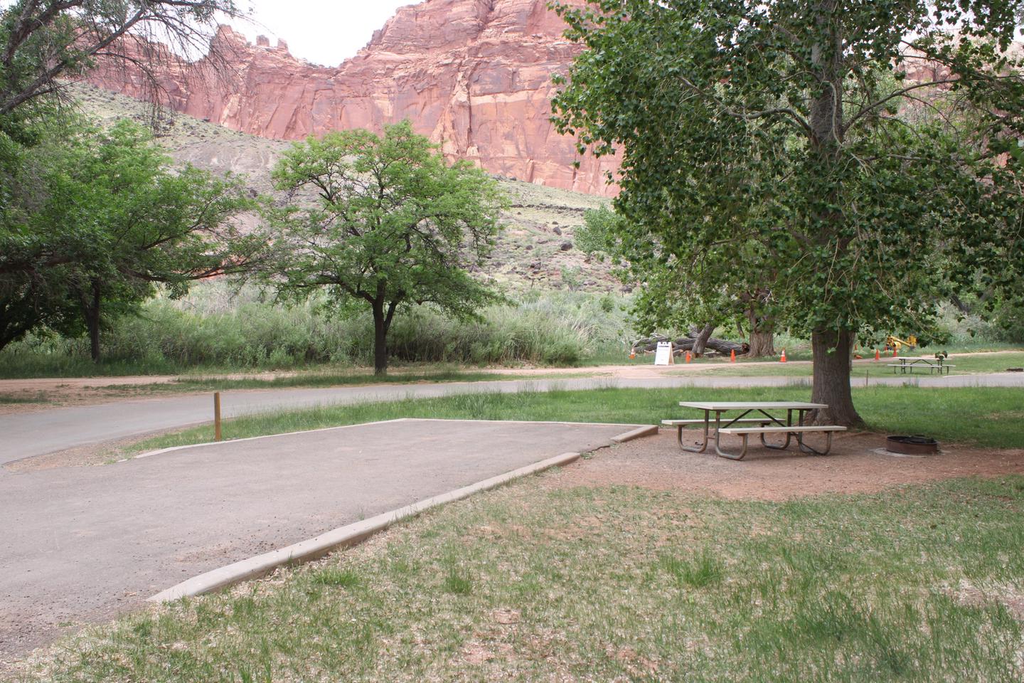 A paved driveway. Facing the end of the driveway, a picnic table and firepit are to the right side. A red cliff towers in the background.Site 30, Loop B in summer.
Paved Dimensions: 15' x 42'