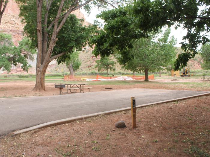 A paved driveway. Facing the end of the driveway, a picnic table, grill, and fire pit are to the left side. A large tree is behind them.Site 42, Loop B in summer.
Paved Dimensions: 23' x 32'