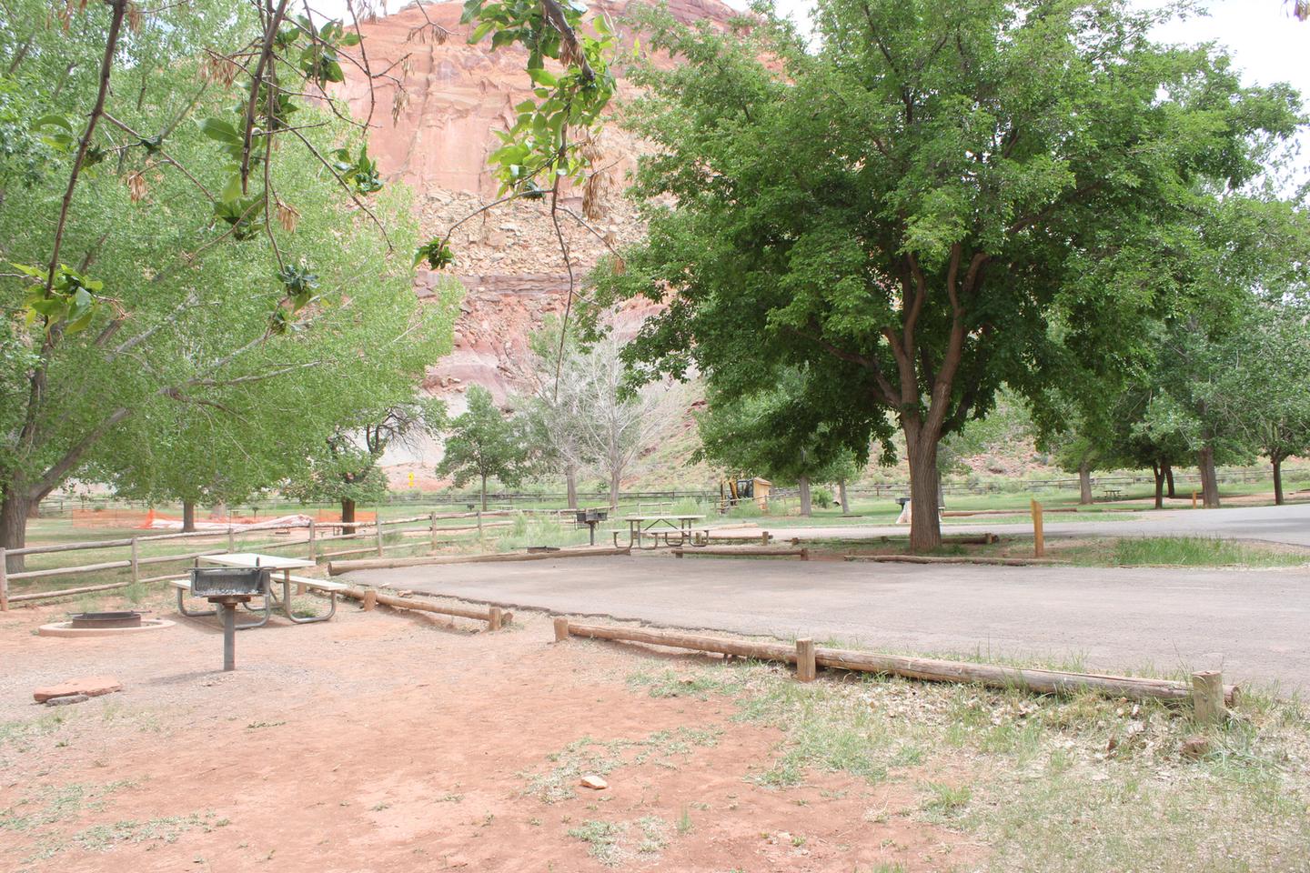 A paved driveway. Facing the end of the driveway, a picnic table, fire pit, and grill are off to the left. A red cliff towers in the background.Site 61, Loop C
Paved Dimensions: 24' x 29'