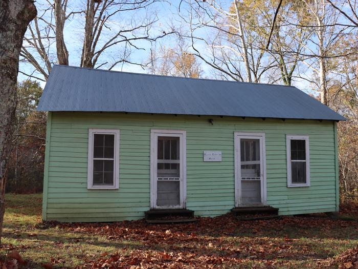 A single story home with two white screen doors and green siding. Autumn leaves cover the ground on the home. Home of Floyd Collins
